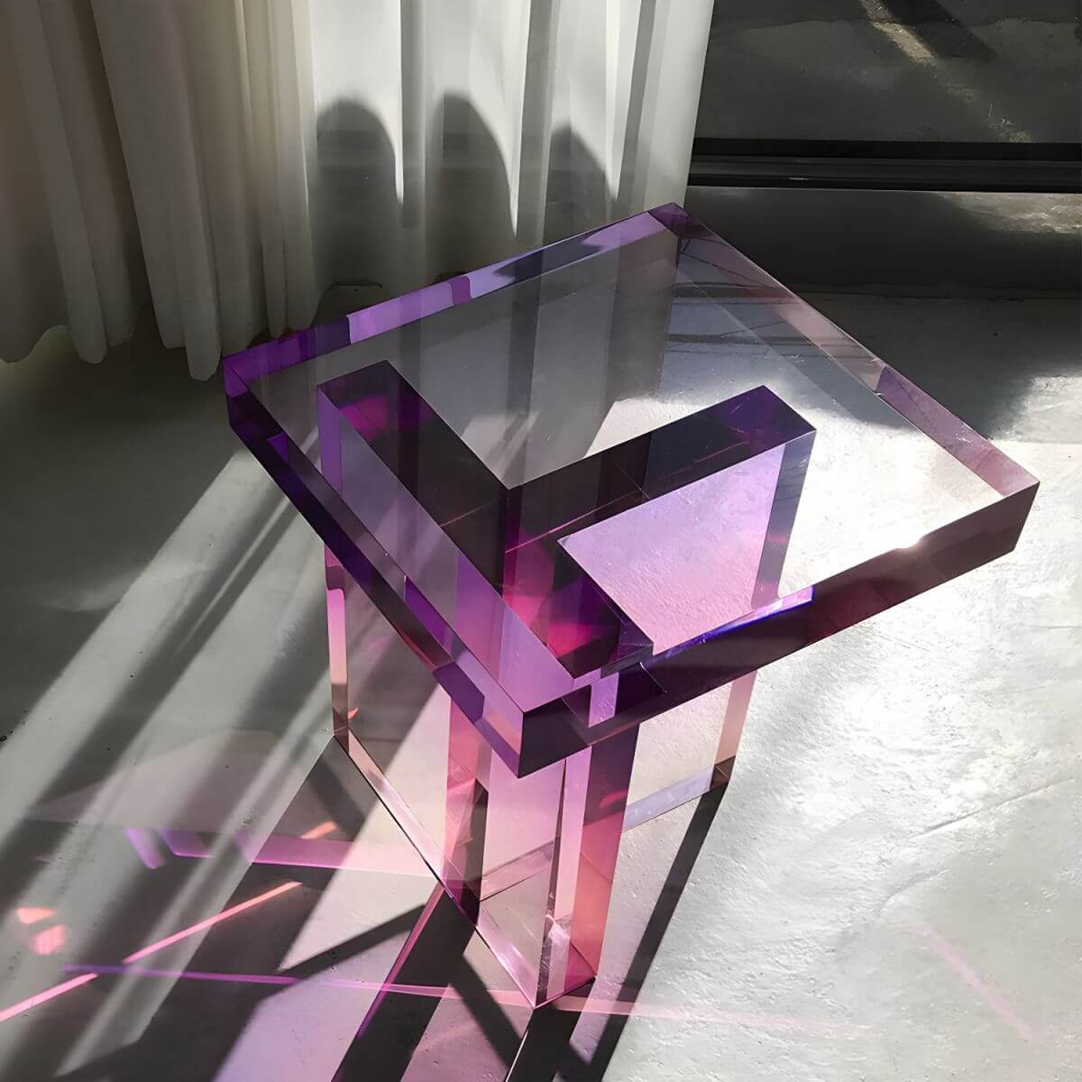 A modernist acrylic side table featuring light refraction geometry and a gloss finish, adding a sculptural and luminous element to a contemporary living space.